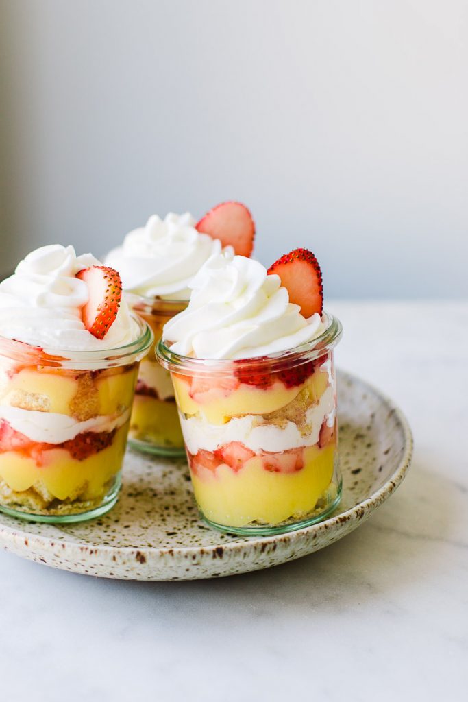 Yellow, white, and red Lemon Strawberry Parfait jars topped with fluffy whipped cream.