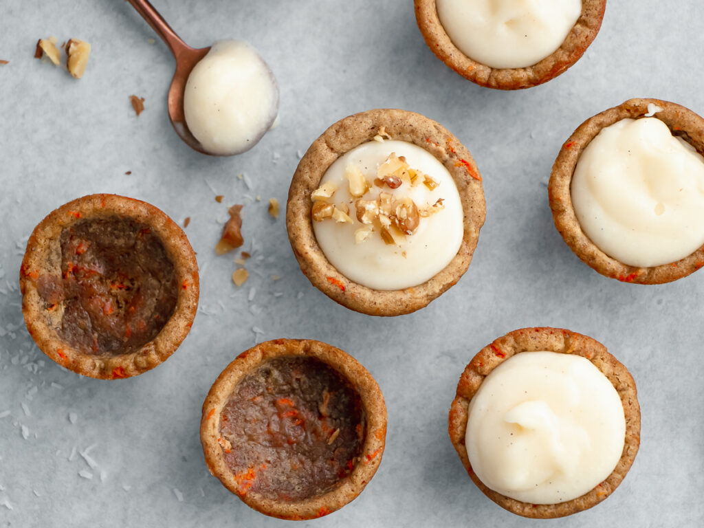 Miniature carrot cake cookie cups are so easy to make with cream cheese frosting in the centers, garnished with walnuts.