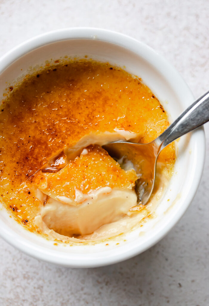 Spoon digging into creamy vanilla custard in a classic creme brulee dish.