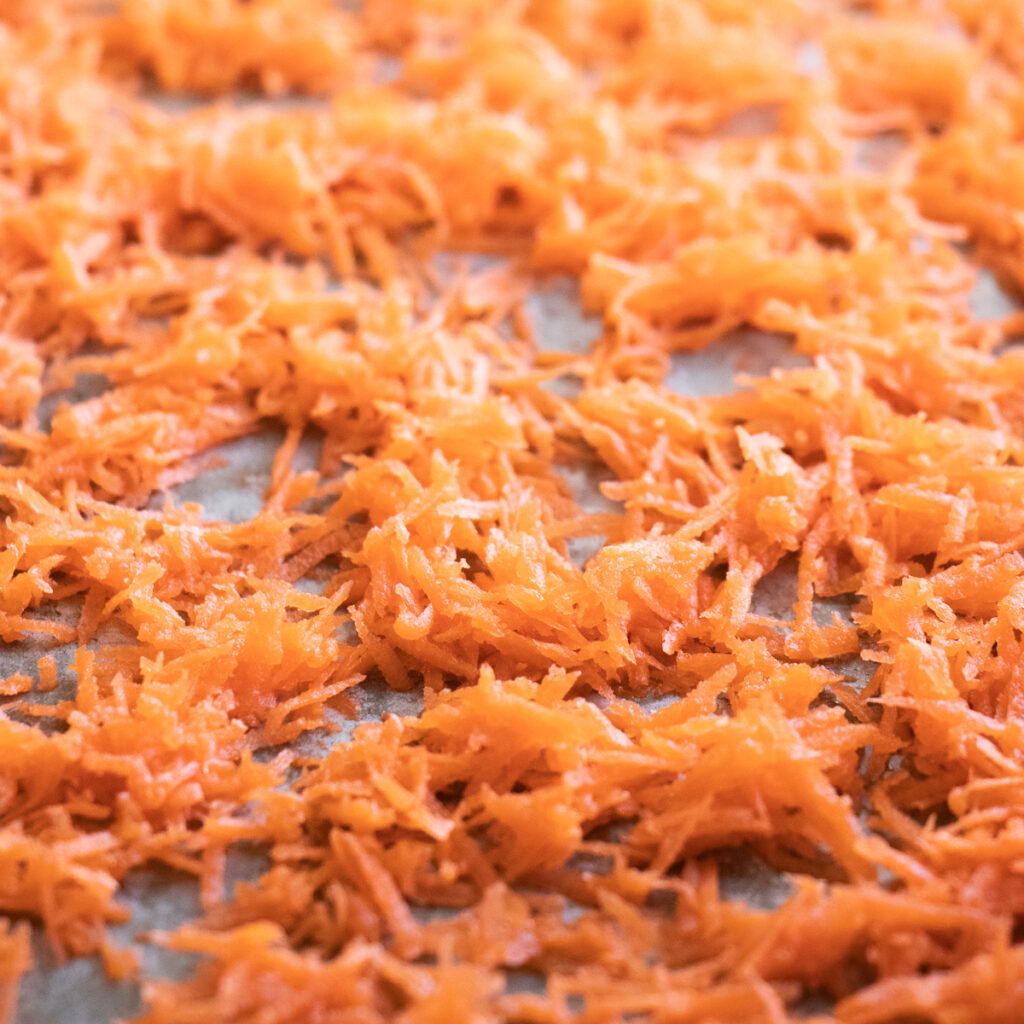 A layer of thinly sliced shredded carrots on a sheet pan before dehydrating in the oven.