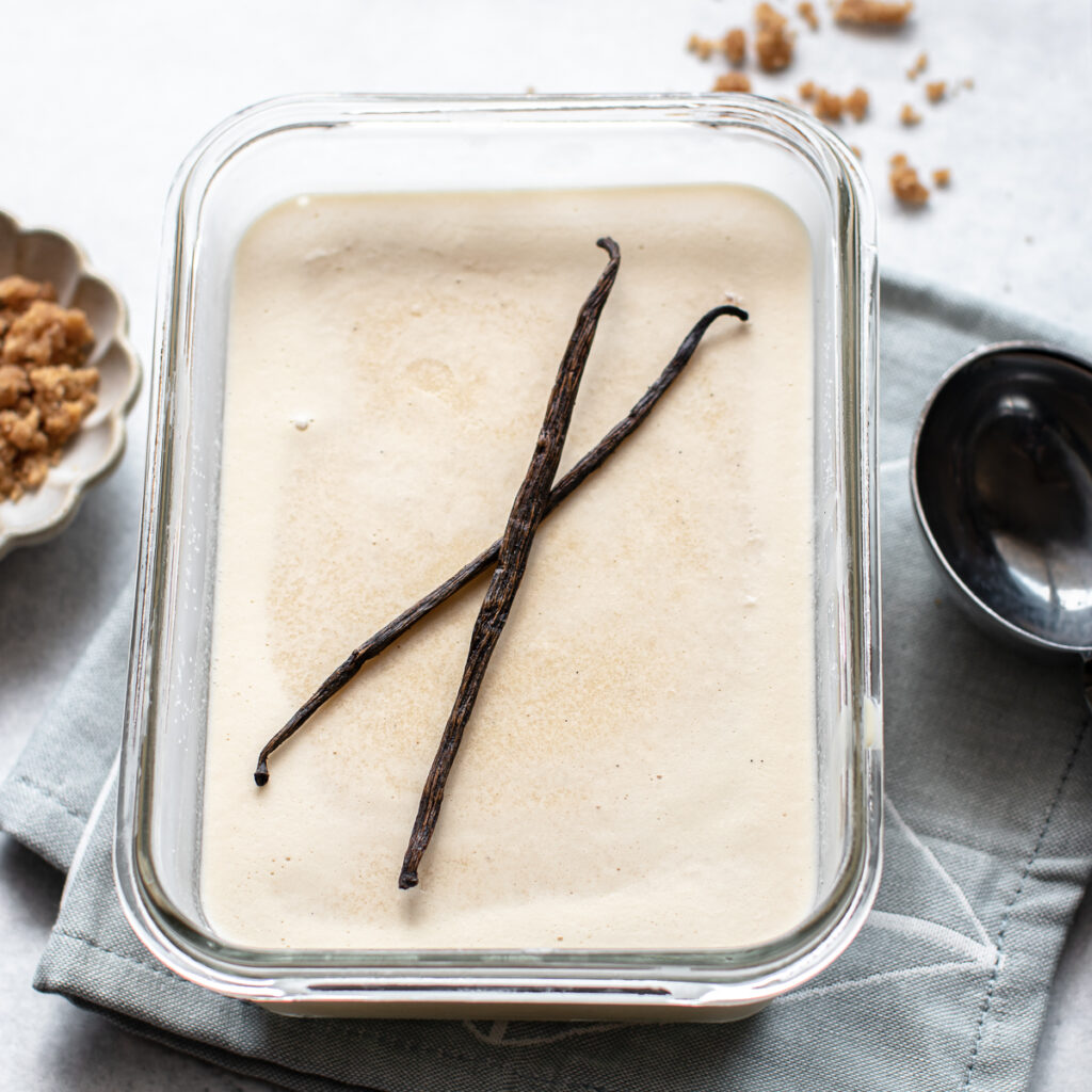 Frozen Vanilla Custard with vanilla beans on top in a glass freezer container.