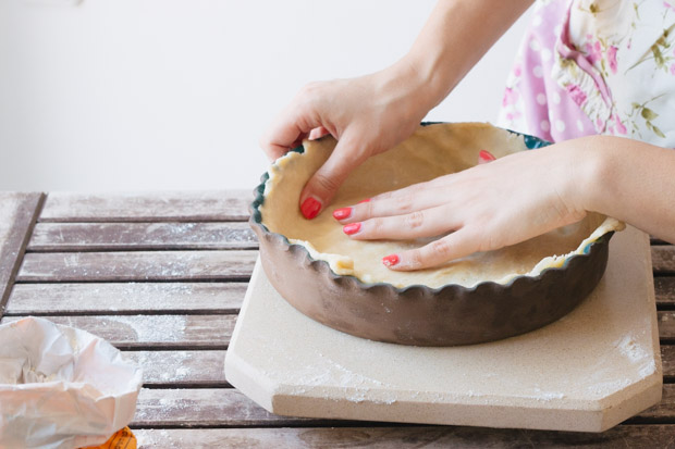 Hands placing a quiche dough into a pie dish.