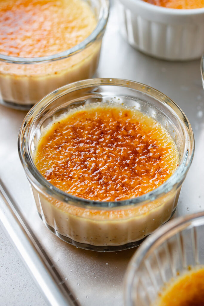 Vanilla creme brulee in a small glass ramekin with golden caramelized sugar on top.