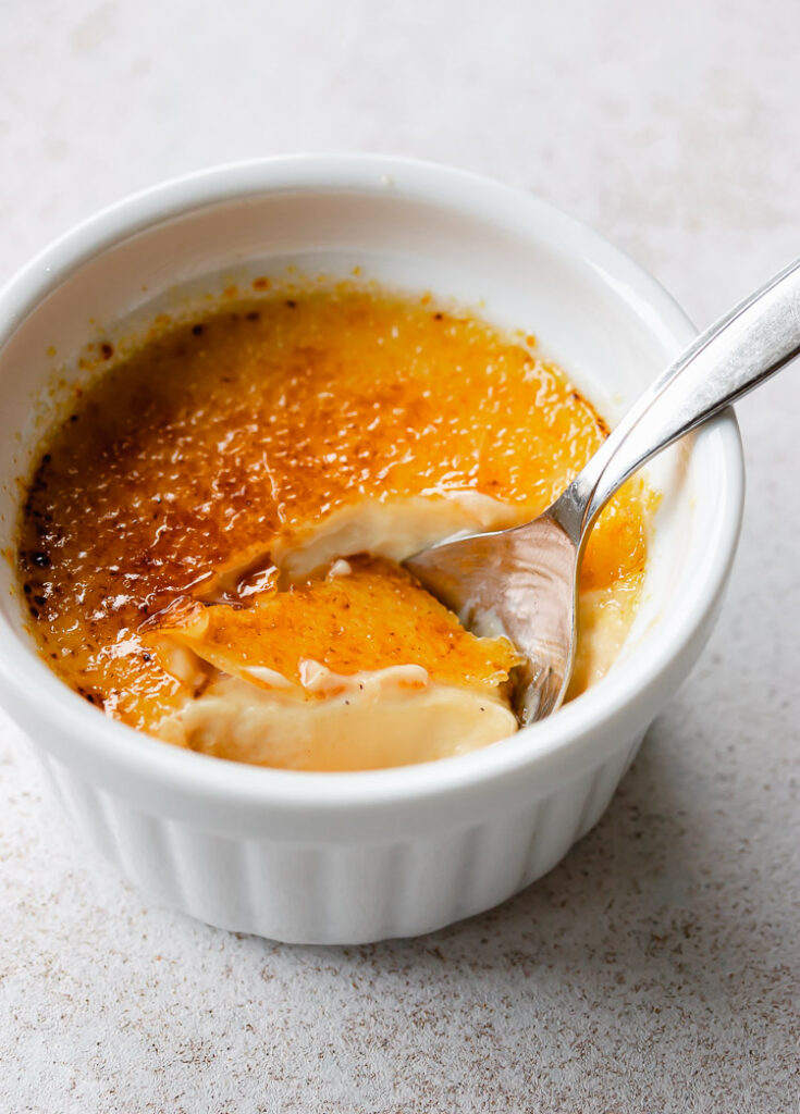 Creamy and smooth, luscious rich vanilla creme brulee with spoon taking a bite of dessert.