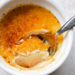 Spoon digging into creamy vanilla custard in a classic creme brulee dish.