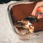 A spoon dipping into a tiramisu dessert.