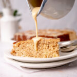 Vanilla sauce slowly being poured over a slice of buttermilk apple cake.