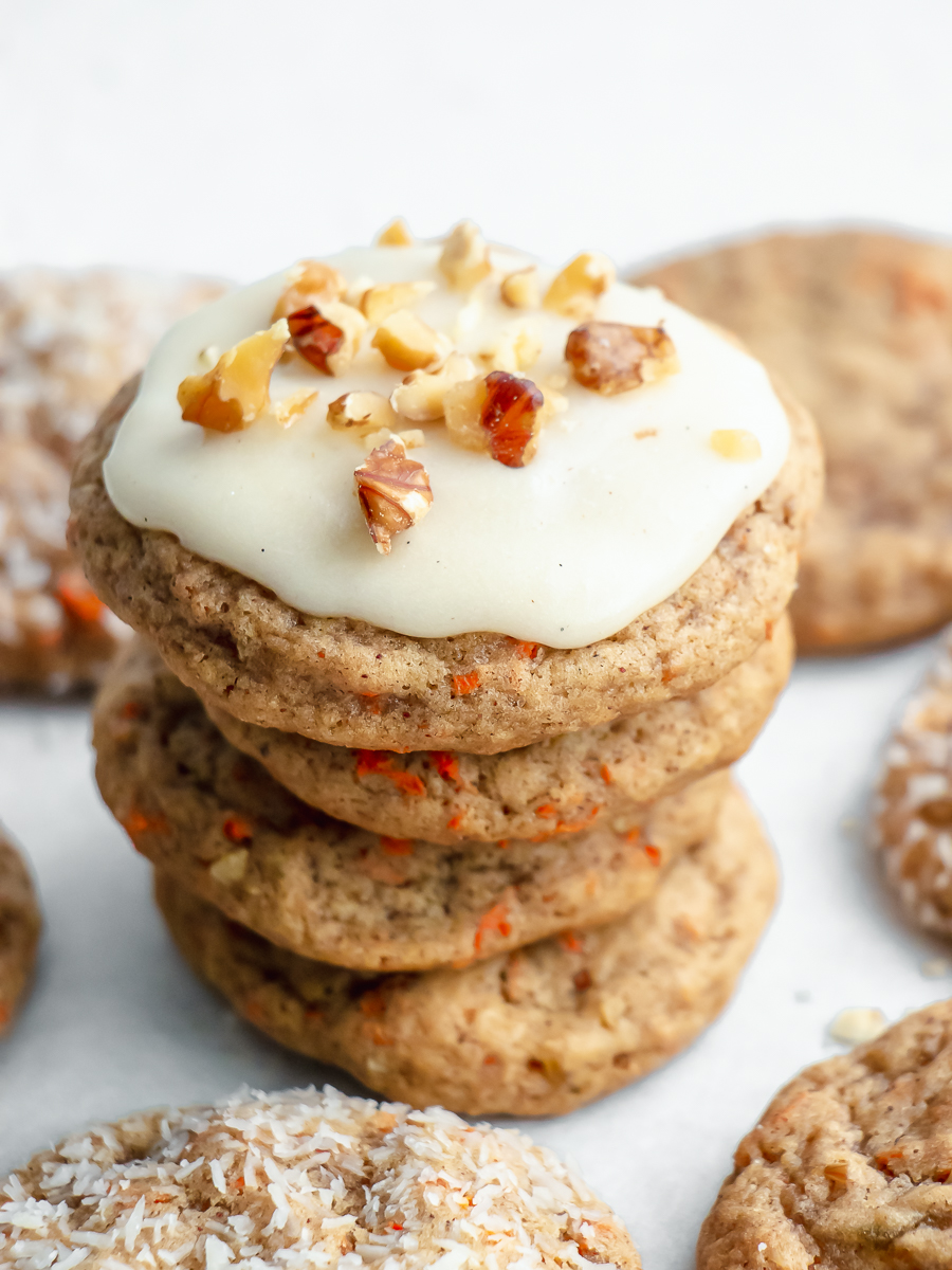 Stack of carrot cake cookies with cream cheese frosting and walnuts on top.