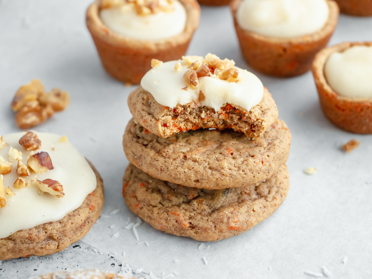 Stack of frosted carrot cake cookies with a bite taken out of the top.