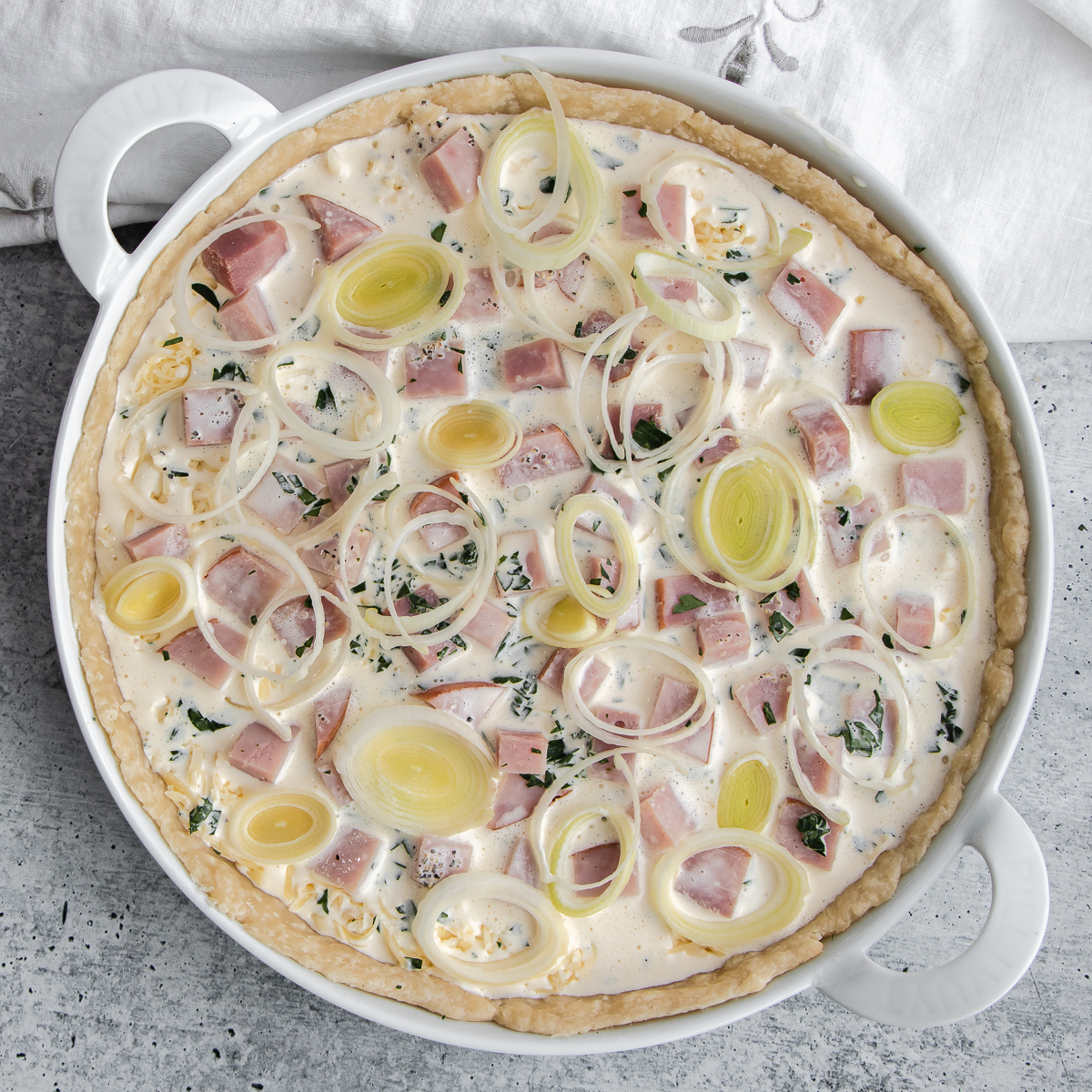 Unbaked ham and cheese quiche topped with leeks.