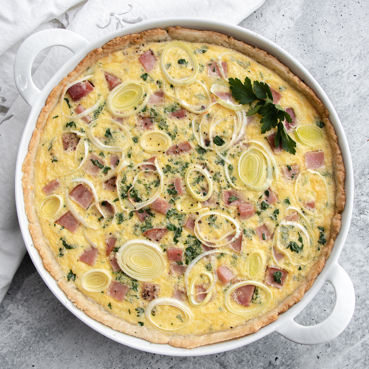 Baked quiche with ham, gruyere and swiss cheeses topped with thinly sliced leeks and chopped fresh parsley.