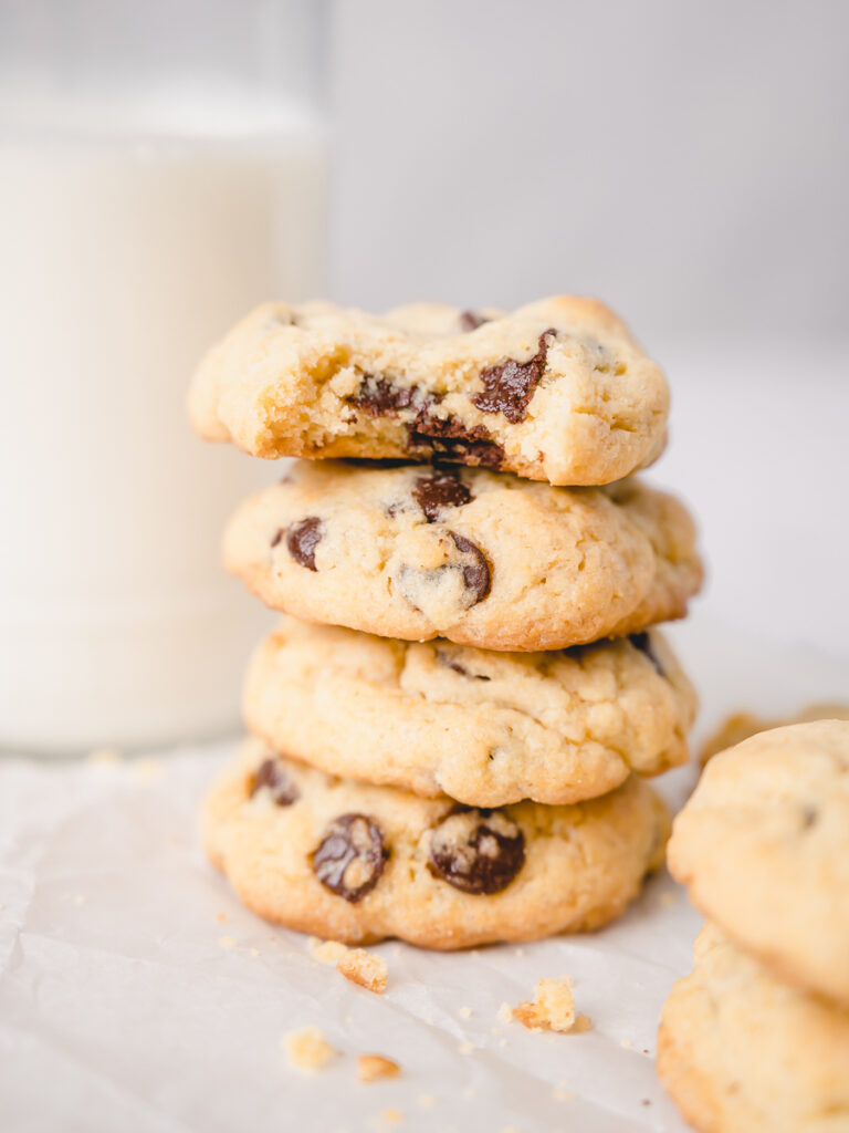 Bite of chocolate chip cookie on a stack of cookies made with vanilla pudding and a glass of milk in the background.