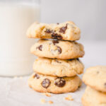 Bite of chocolate chip cookie on a stack of cookies made with vanilla pudding and a glass of milk in the background.