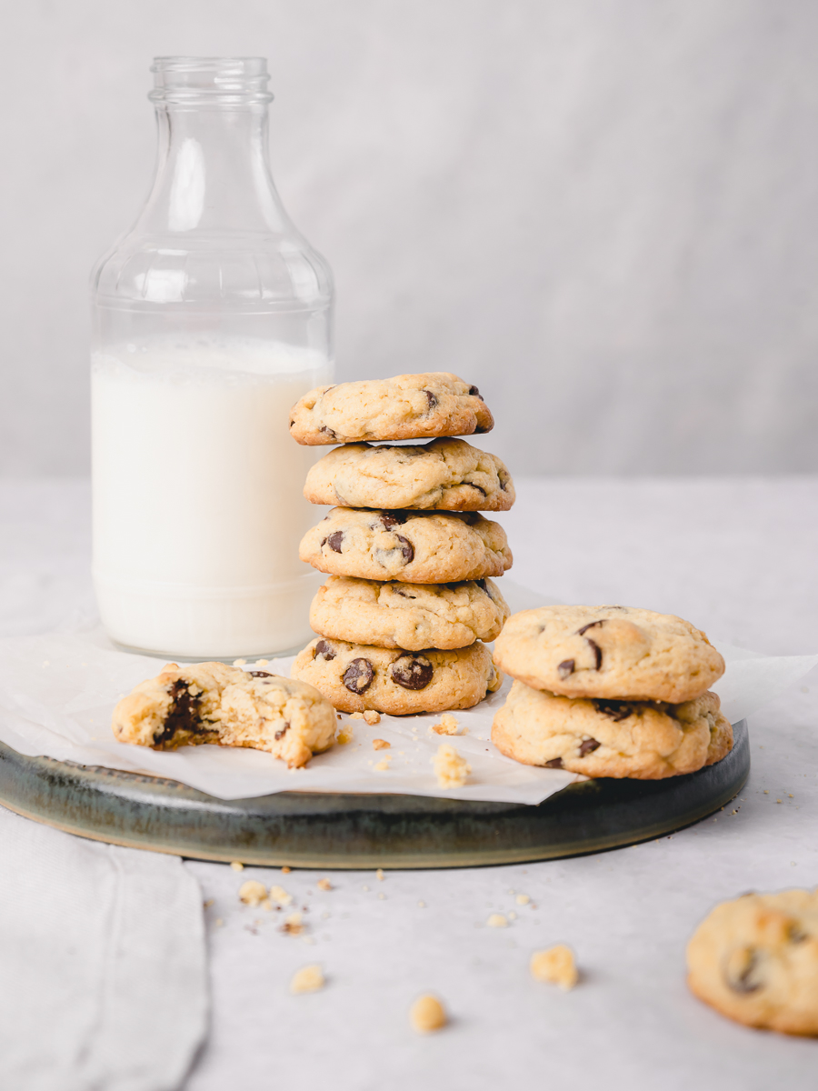 Stack of vanilla pudding chocolate chip cookies and a glass of milk in the background.