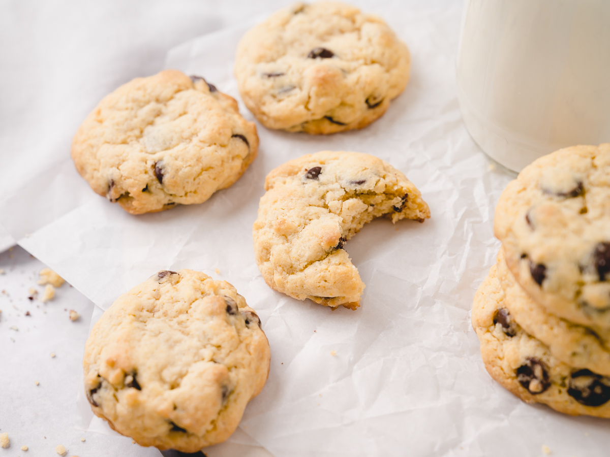 An array of chocolate chip cookies on parchment paper and a glass of milk.