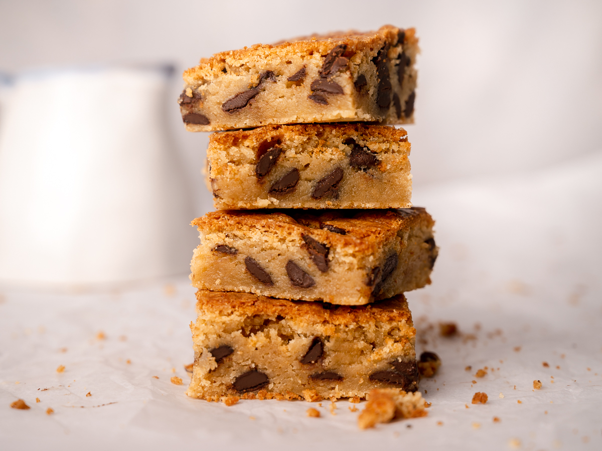 Chocolate chip cookie blondie bars with fudgy middles showing in a stack of four bars.