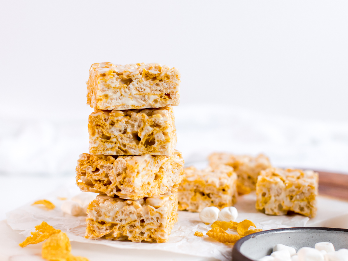 Tower of cornflake rice crispy marshmallow treats with corn flakes and marshmallows scattered.