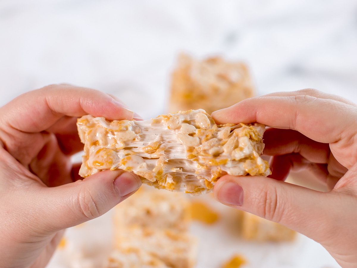 Two hands stretching marshmallow crispy treats apart.