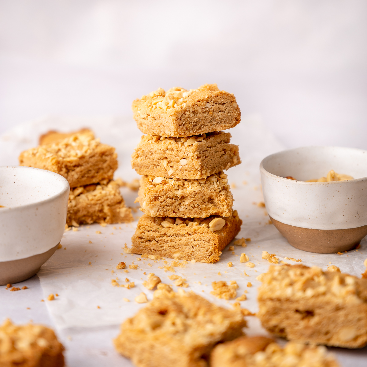 Stack of four peanut butter blondie bars with peanuts scattered.