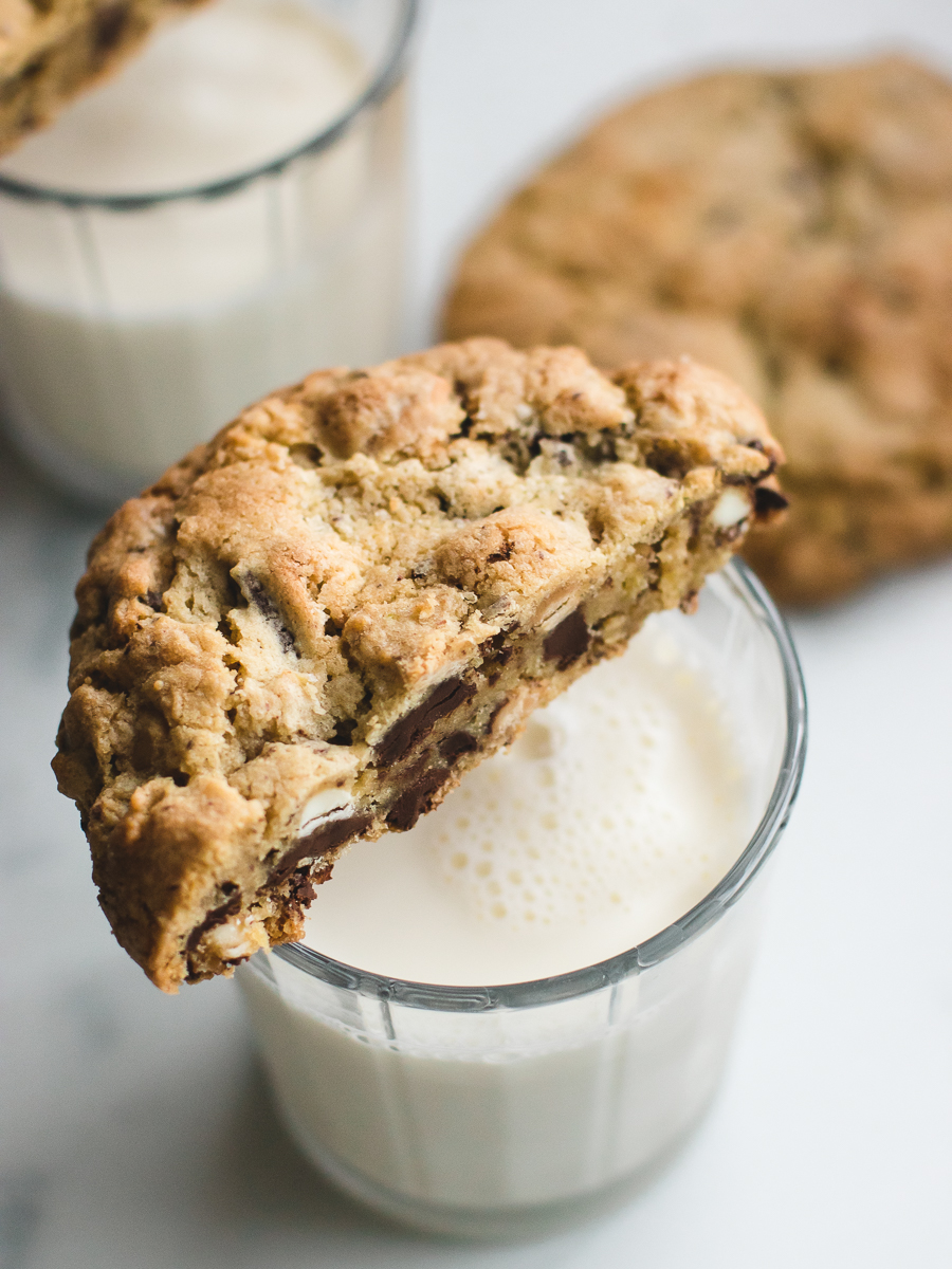 Kitchen sink cookie with various white and dark chocolate chips over a glass of milk.