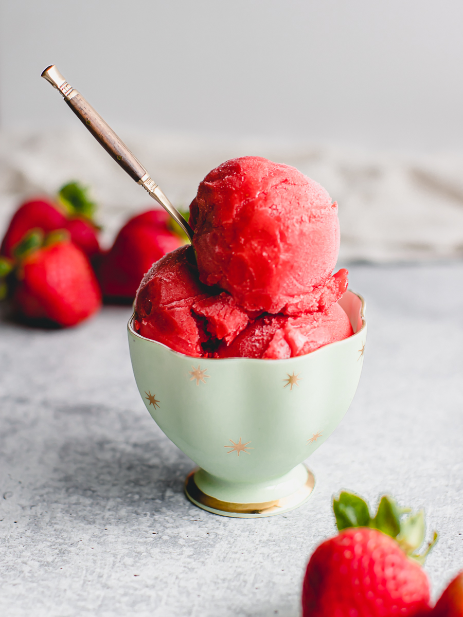 Scoops of frozen strawberry custard in a vintage teacup surrounded by fresh strawberries.