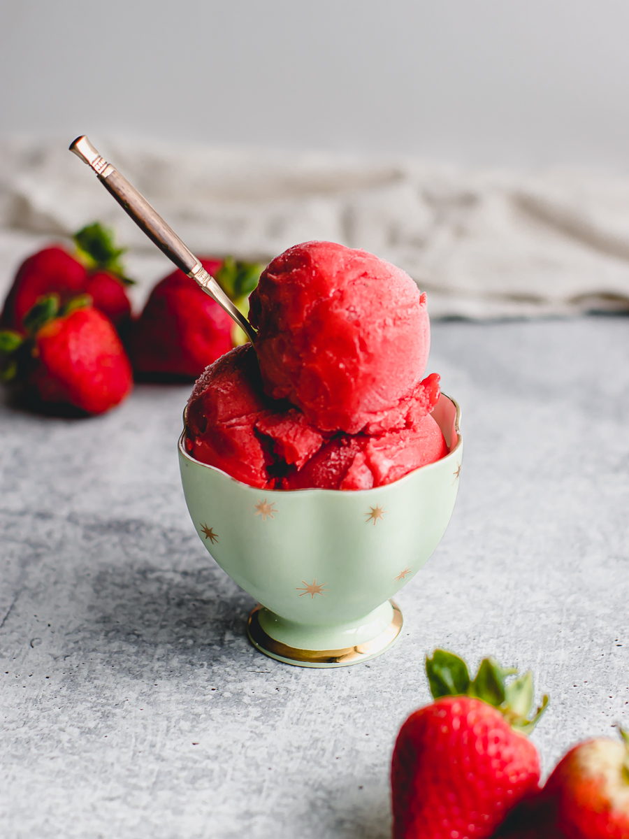 Scoops of frozen strawberry custard in a vintage teacup surrounded by fresh strawberries.