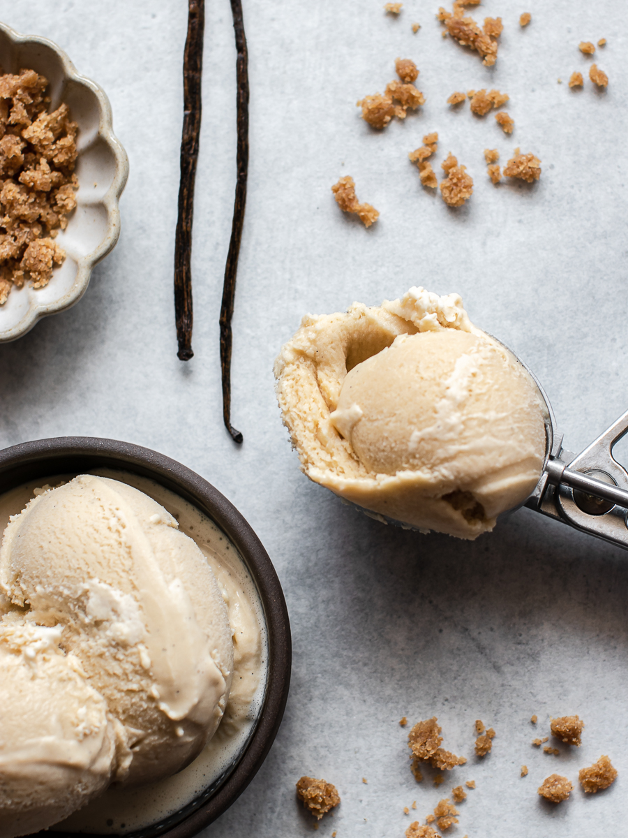 Vanilla bean brown sugar frozen custard in a bowl and an ice cream scoop with vanilla beans in the background.