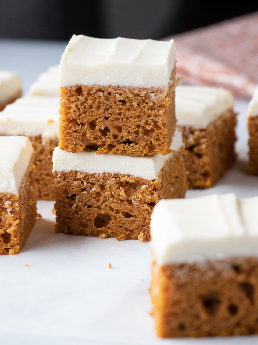 Pumpkin bars with thick layer of cream cheese frosting stacked on top of each other.