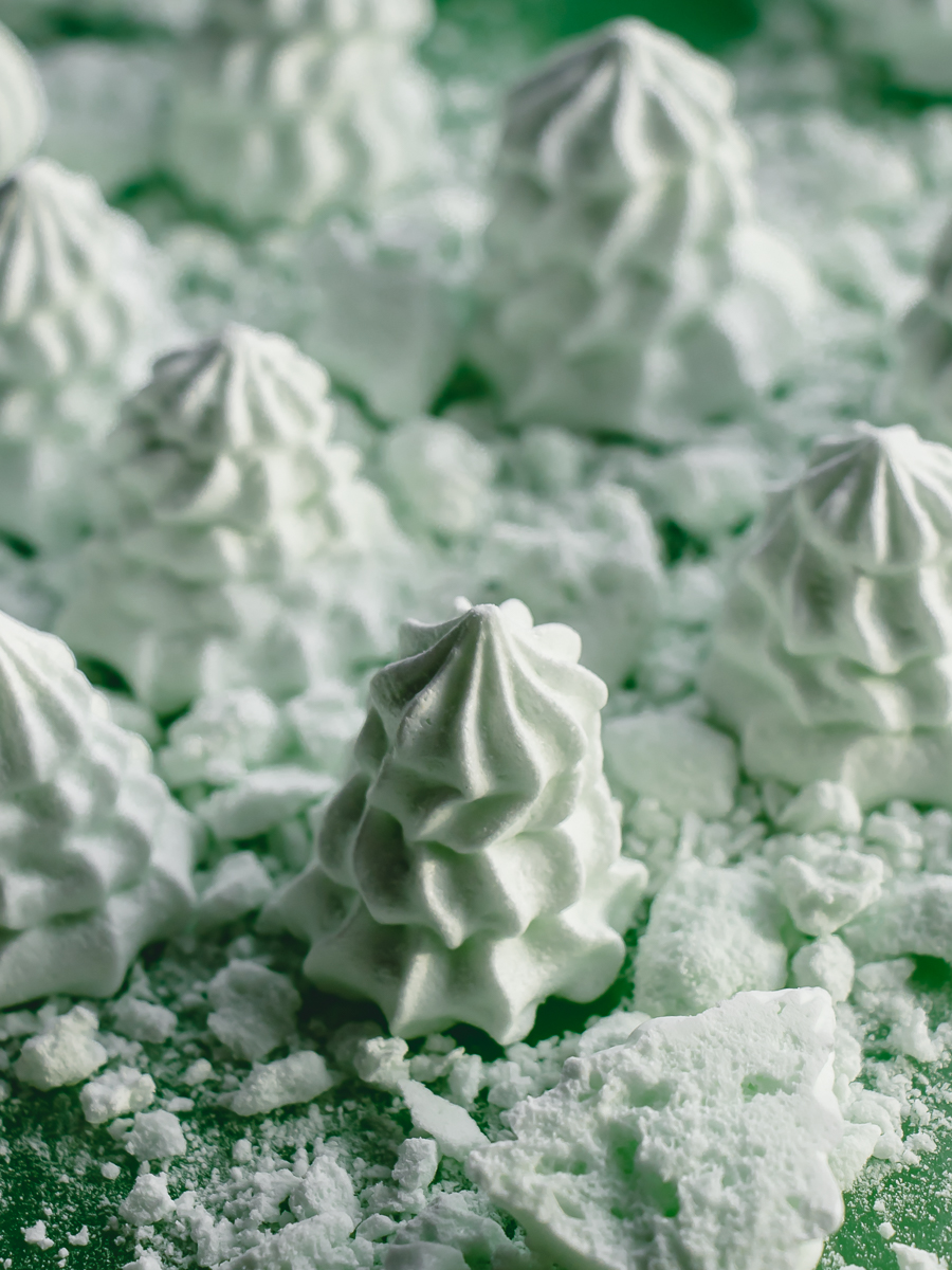 Mint meringue cookies in the shape of Christmas trees with crumbled meringues forming edible snow.