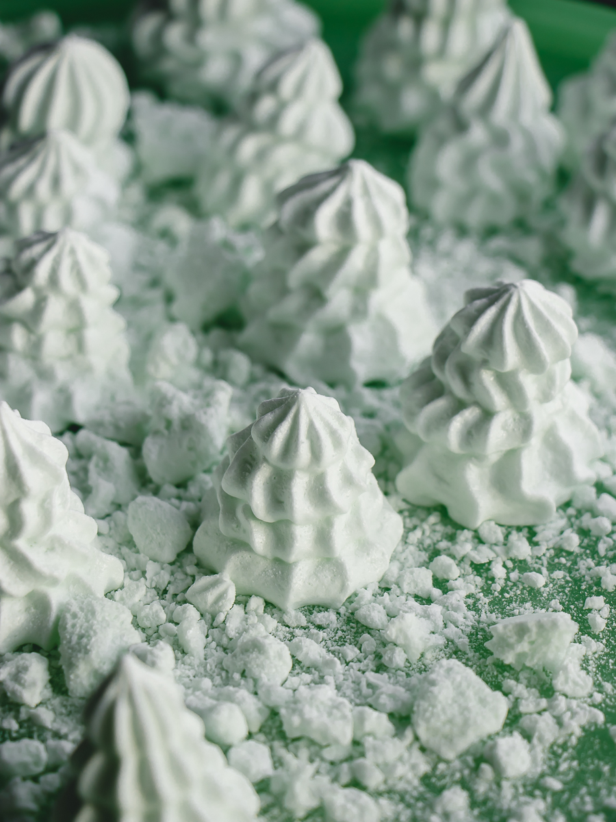 Mint meringue cookies in the shape of Christmas trees with crumbled meringues forming edible snow.