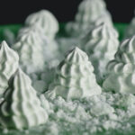 Mint meringue cookies in the shape of Christmas trees with crumbled meringues forming edible snow.