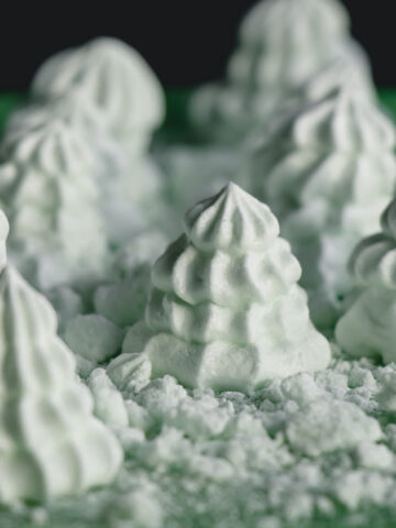 Mint meringue cookies in the shape of Christmas trees with crumbled meringues forming edible snow.